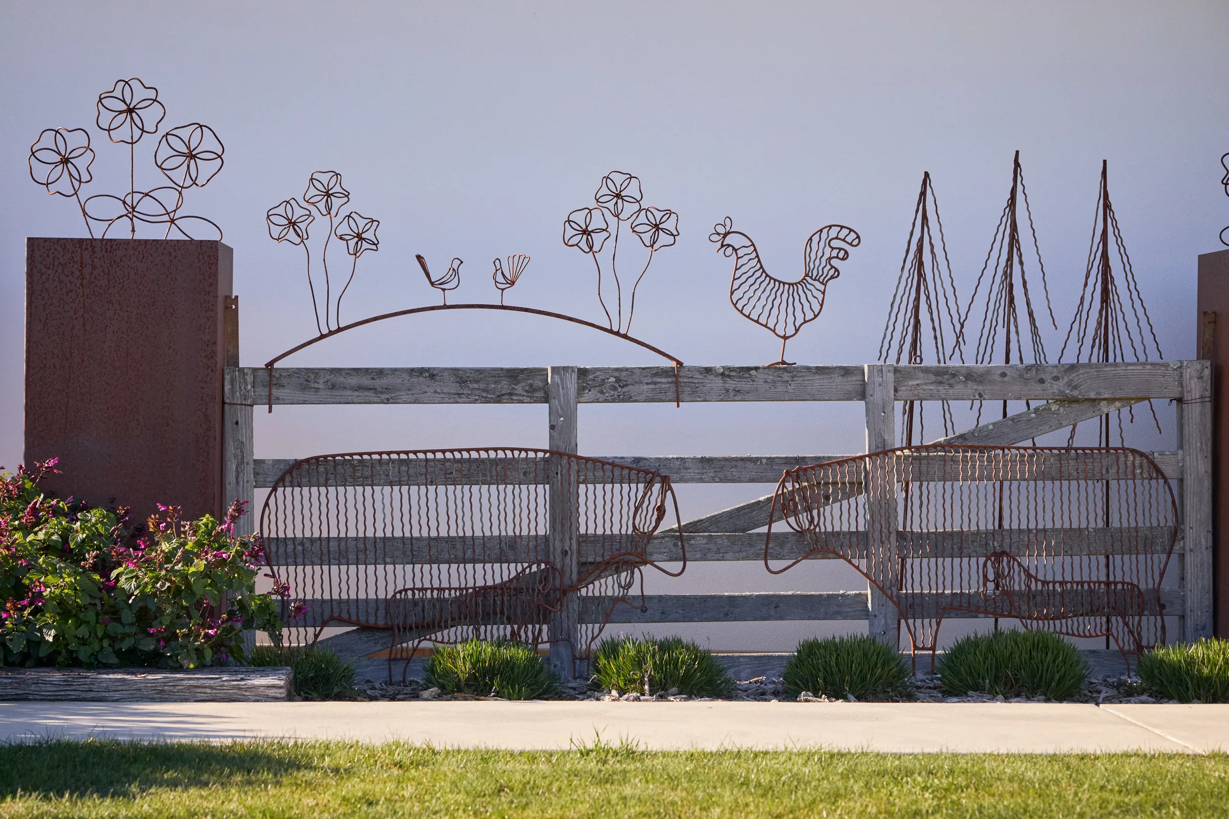 A wire sheep sculpture on a post-and-rail fence.