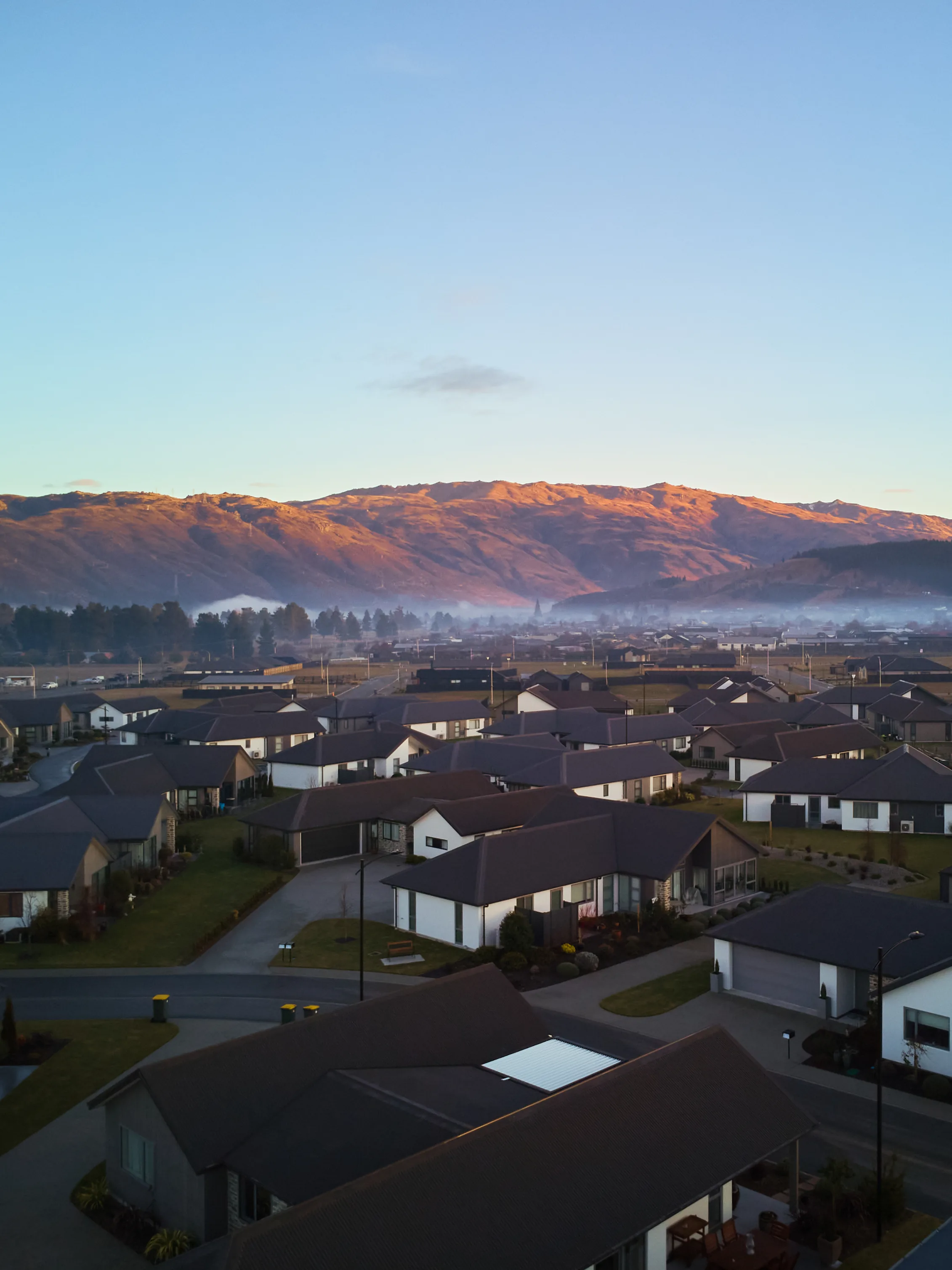 The village at first light, with the Dunstan range lit gold above it and Clyde township under mist behind.