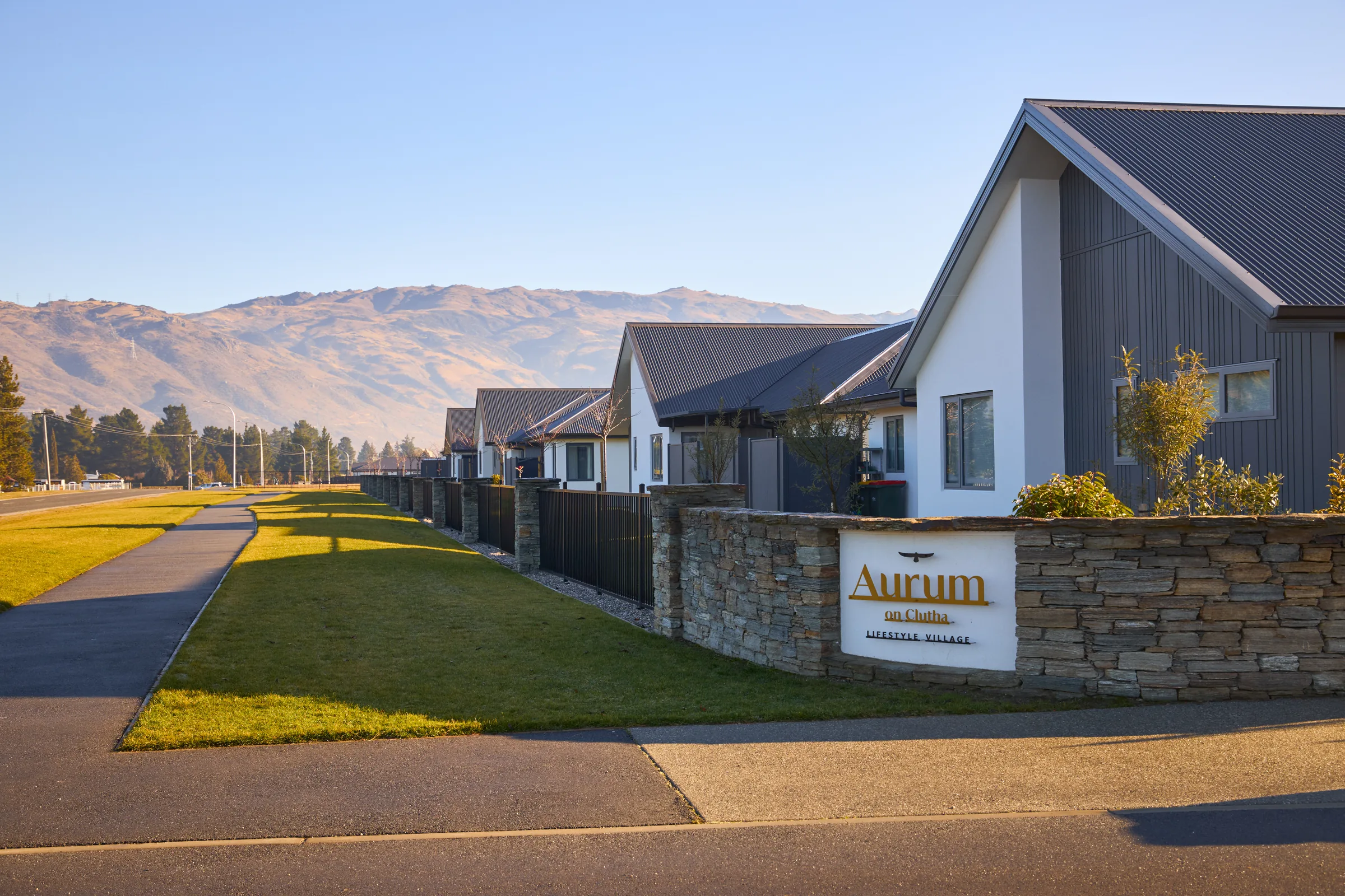 Aurum on Clutha's schist entrance wall, with the village street beyond it.