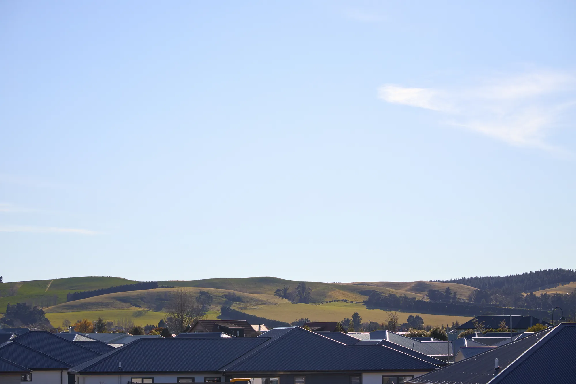Rooflines of village homes against pastoral hills under a clear sky.