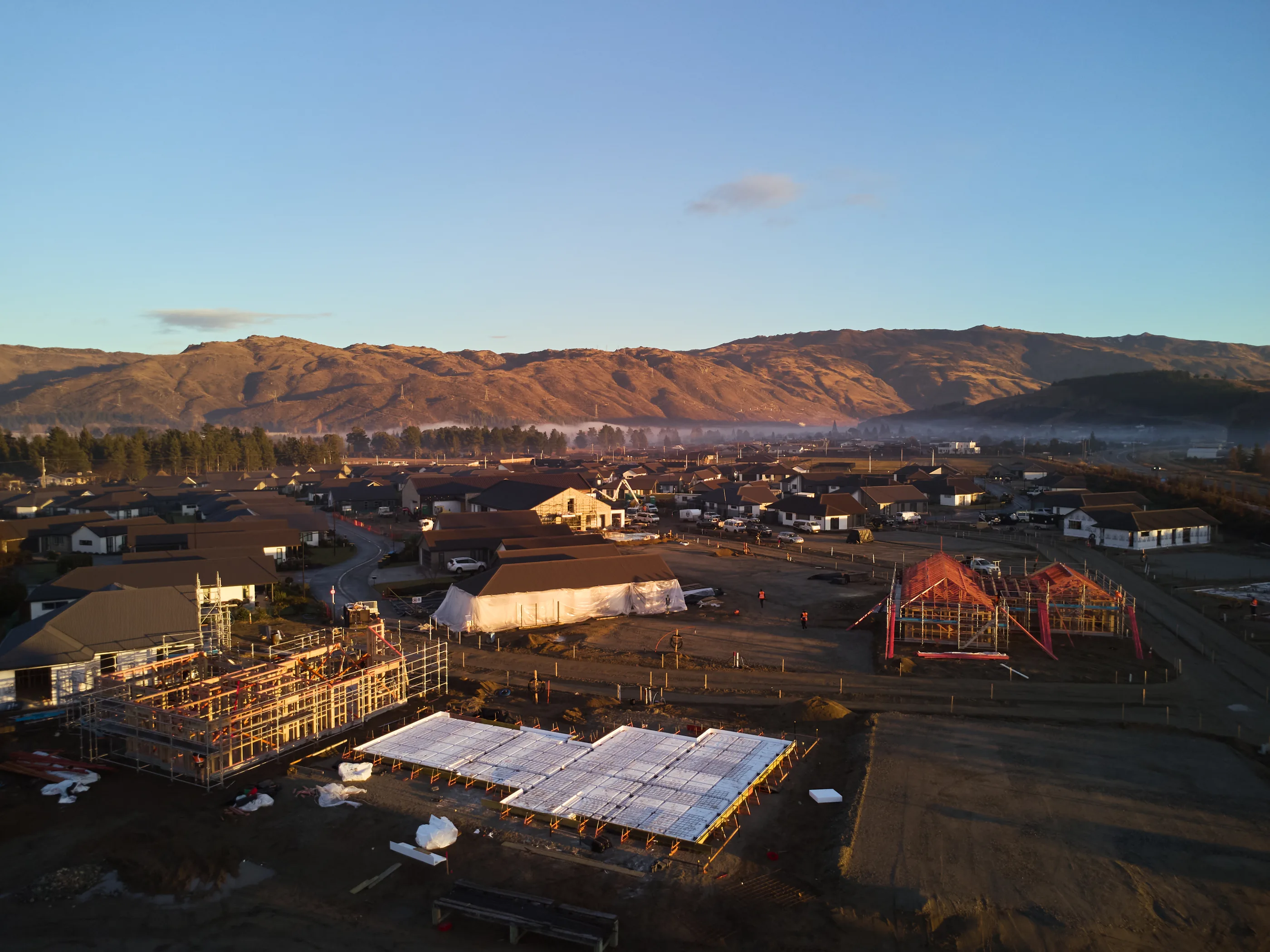 New homes taking shape on site, scaffolding and framing catching the last light.